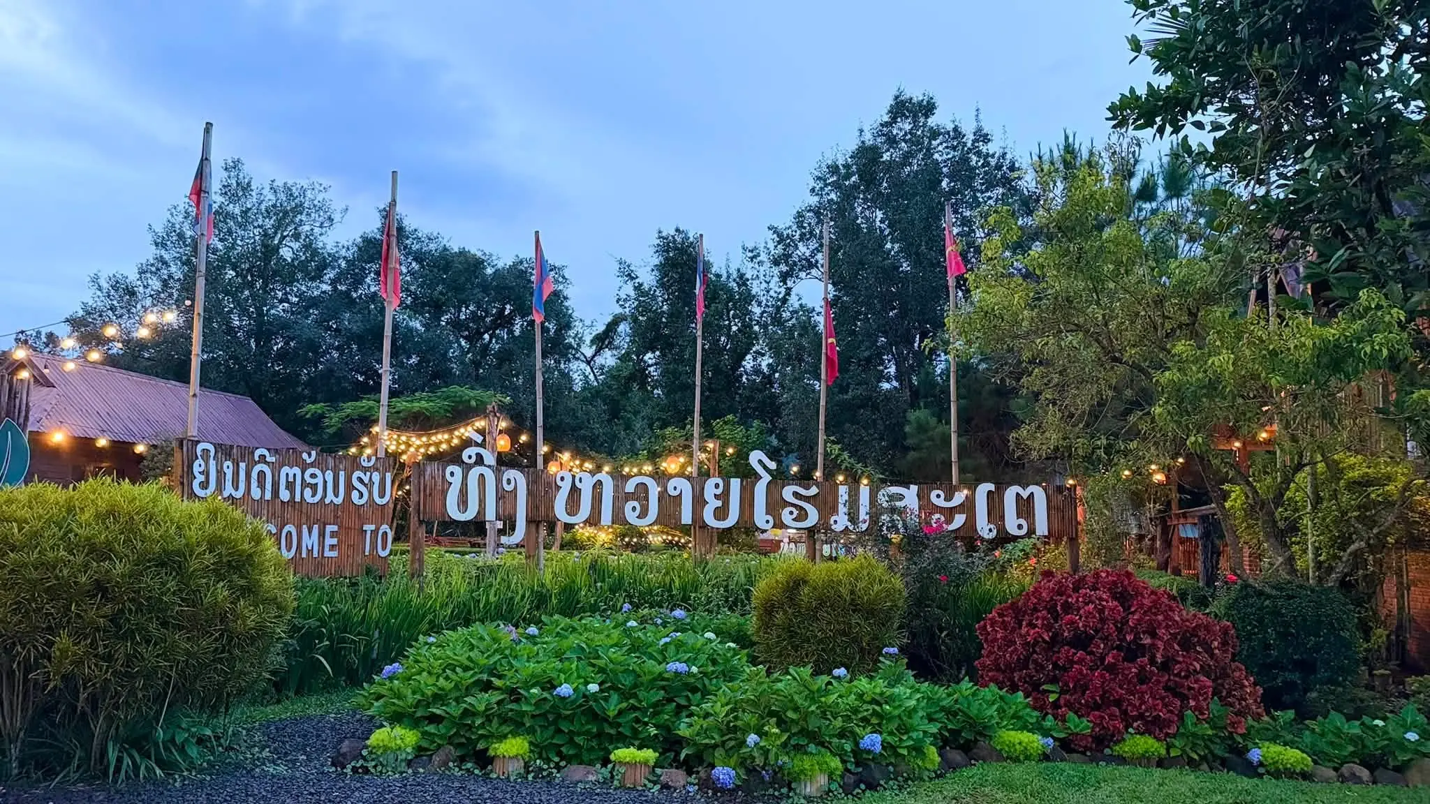 ป้ายทางเข้าทุ่งหวายโฮมสเตย์ ยามค่ำ พร้อมสวนดอกไม้และไฟราว